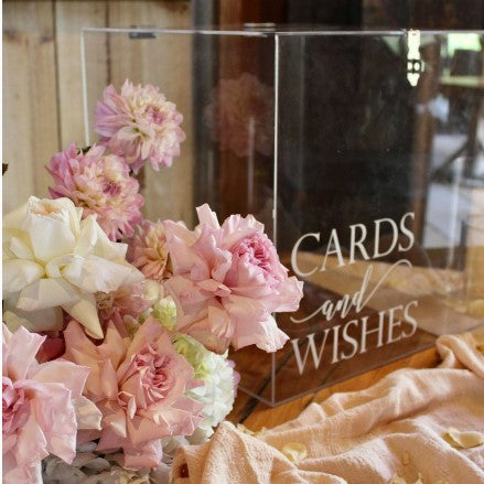 Clear acrylic 'Cards and Wishes' sign with pink flowers on a wooden surface.