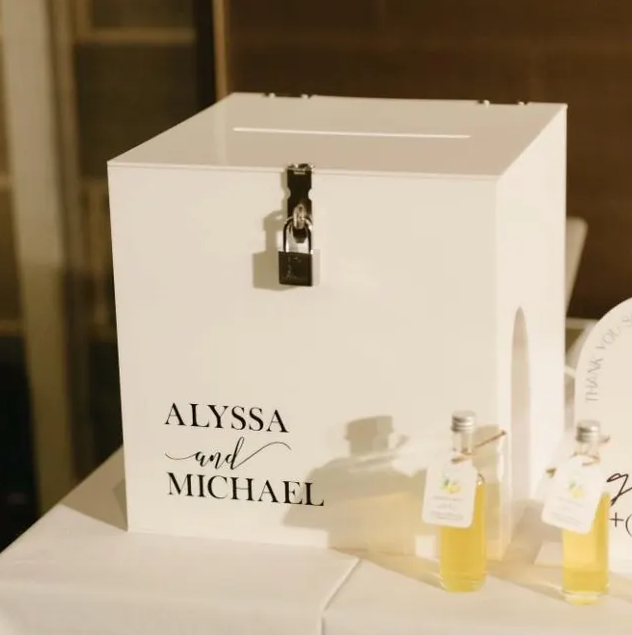 White box with 'Alyssa and Michael' text, lock, and bottles on a table.