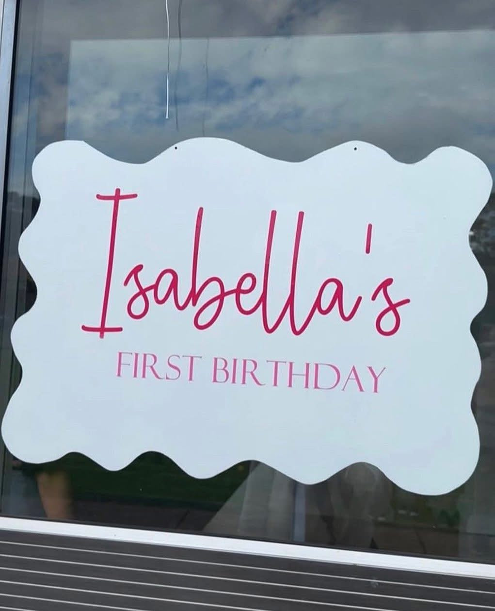 Decorative window sticker with 'Isabella's First Birthday' text on a glass surface.