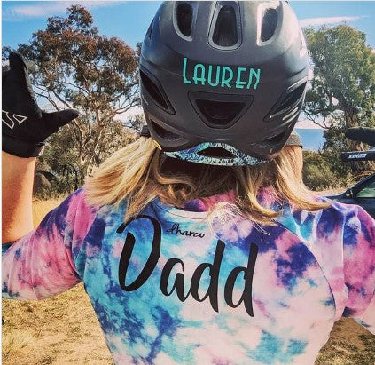 Person wearing a tie-dye shirt with 'Dadd' and a helmet with 'LAUREN' on it, outdoors.