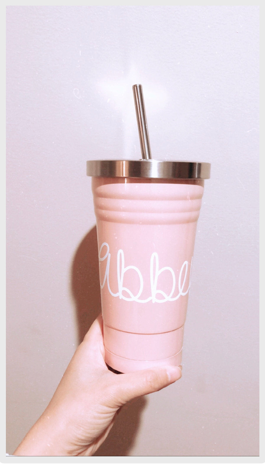 Pink tumbler with silver lid and straw held by a hand against a light background